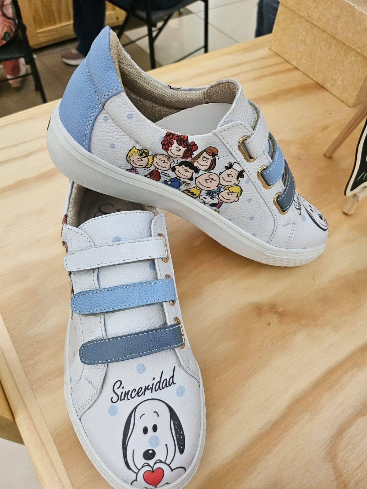 Par de sneakers de cuero con tiras celestes y un grupo de personajes ilustrados