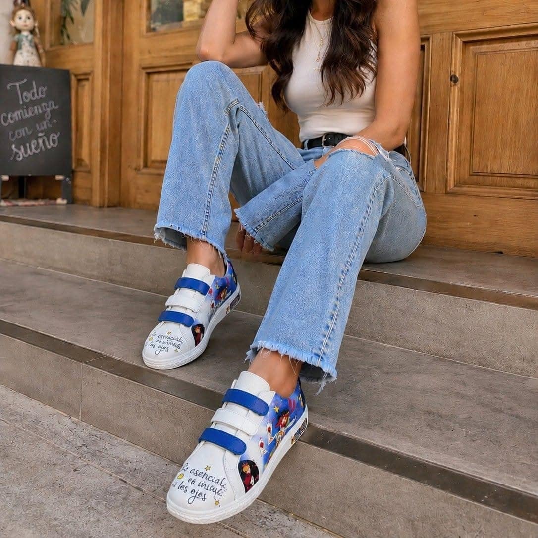 Mujer sentada en unas gradas de madera con jeans claros, calzando los sneakers de tiras azules
