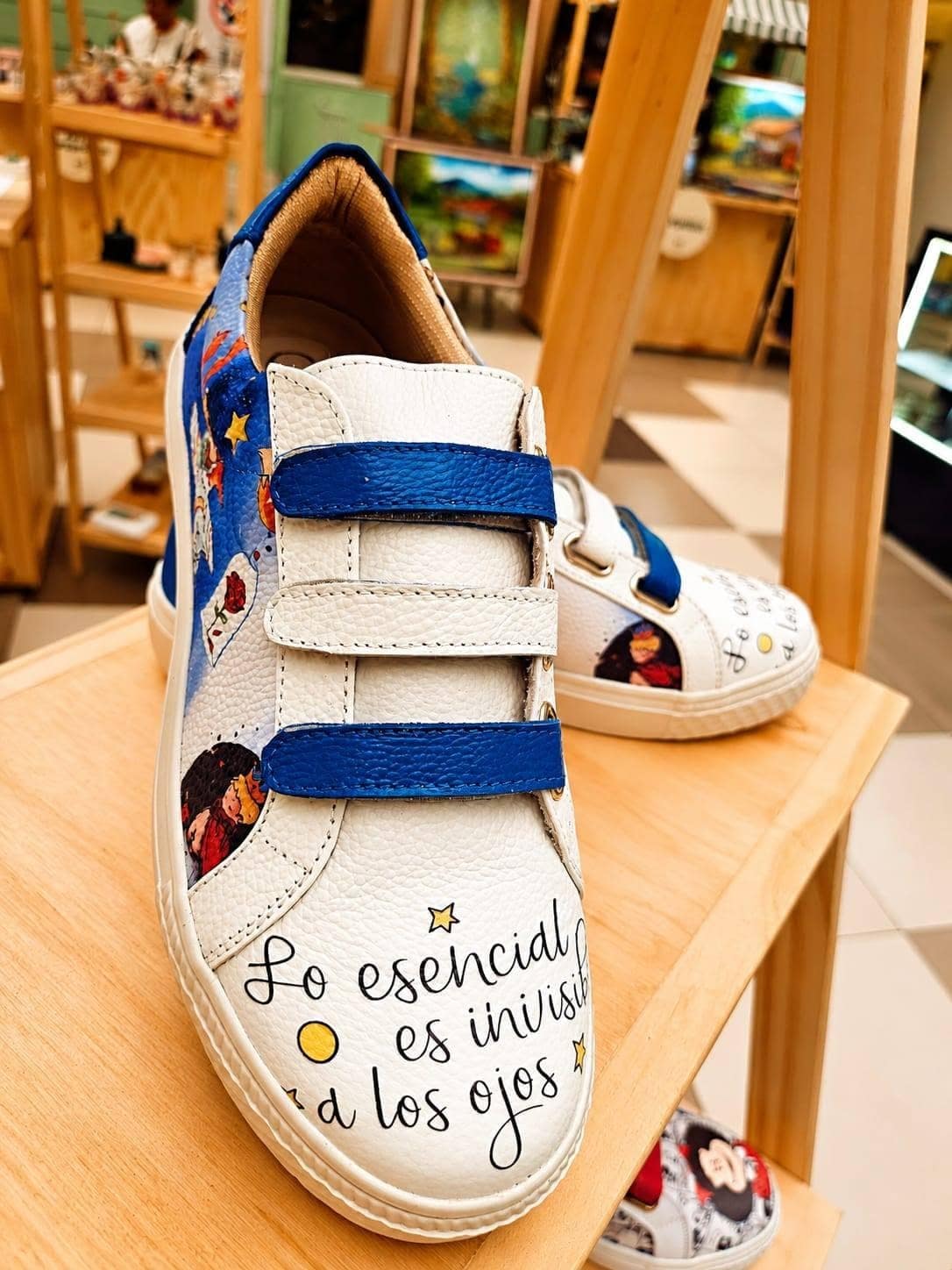 Par de sneakers de cuero blanco con tiras azul marino sobre una repisa de madera clara