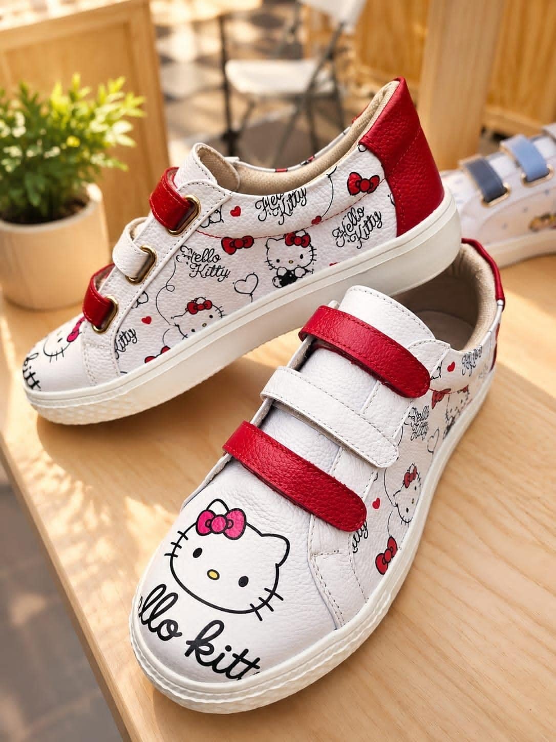 Par de sneakers de cuero blanco con tiras rojas y estampado repetido, sobre repisa de madera